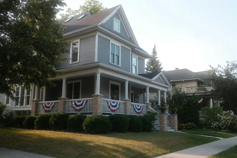 A gray two-story house with red, white and blue bunting along the porch rail