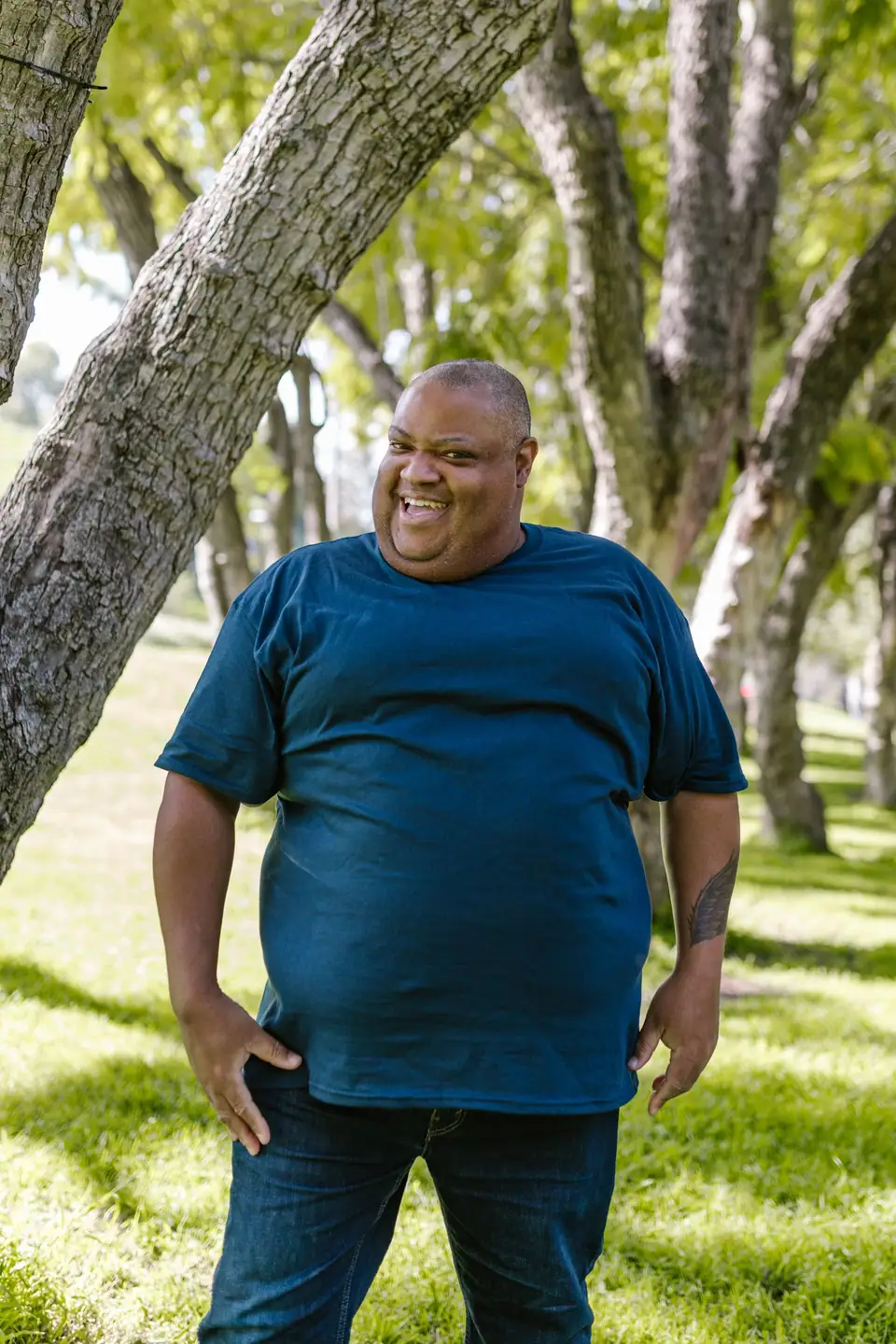 A smiling man in a blue crew-neck T-shirt among trees