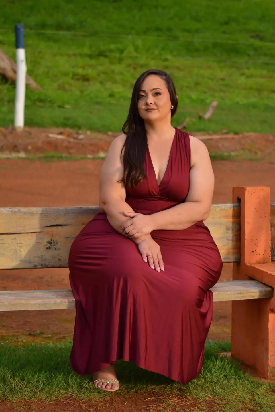 A woman in a long red dress sitting on a park bench